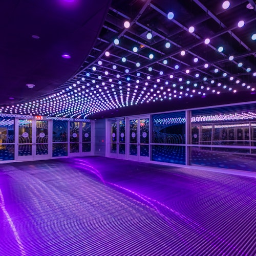 Una sala con pisos y paredes reflectantes iluminada por numerosas pequeñas luces LED de color púrpura y azul, dispuestas en patrones.