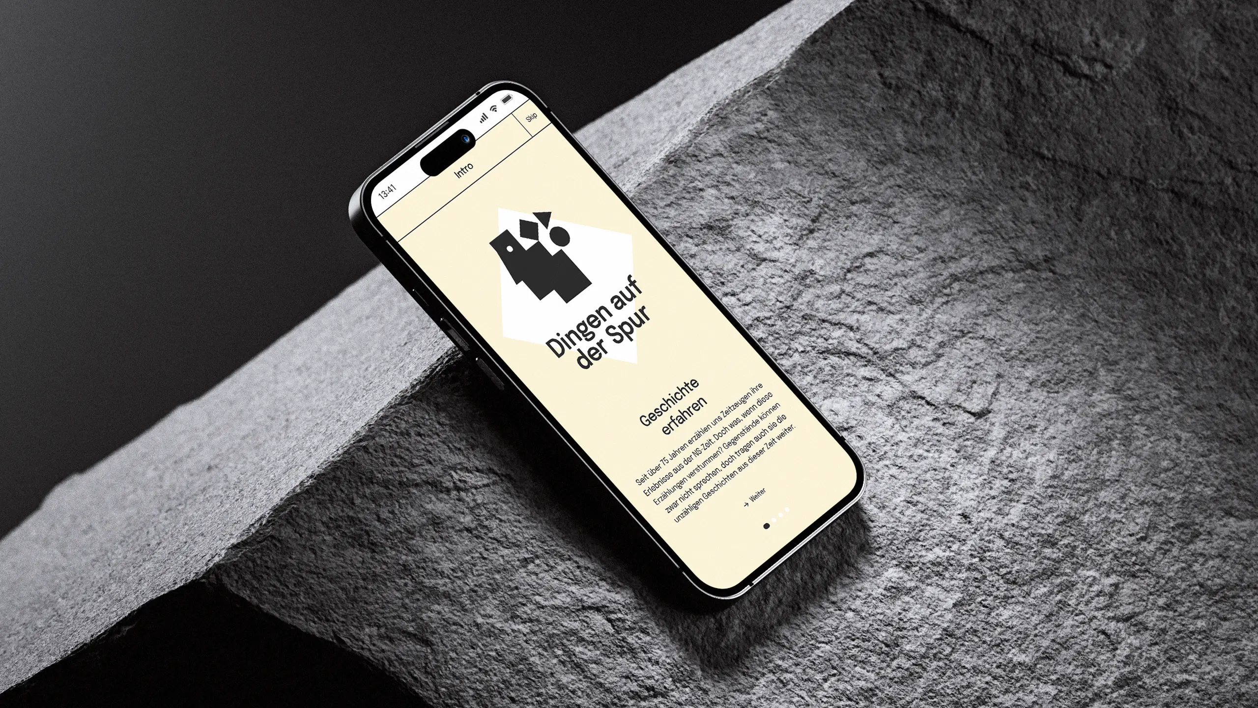 Smartphone-Mockup auf Stein mit Intro-Screen „Dingen auf der Spur – Geschichte erfahren“ und Text zu Zeitzeugen und Gegenständen der NS-Zeit.