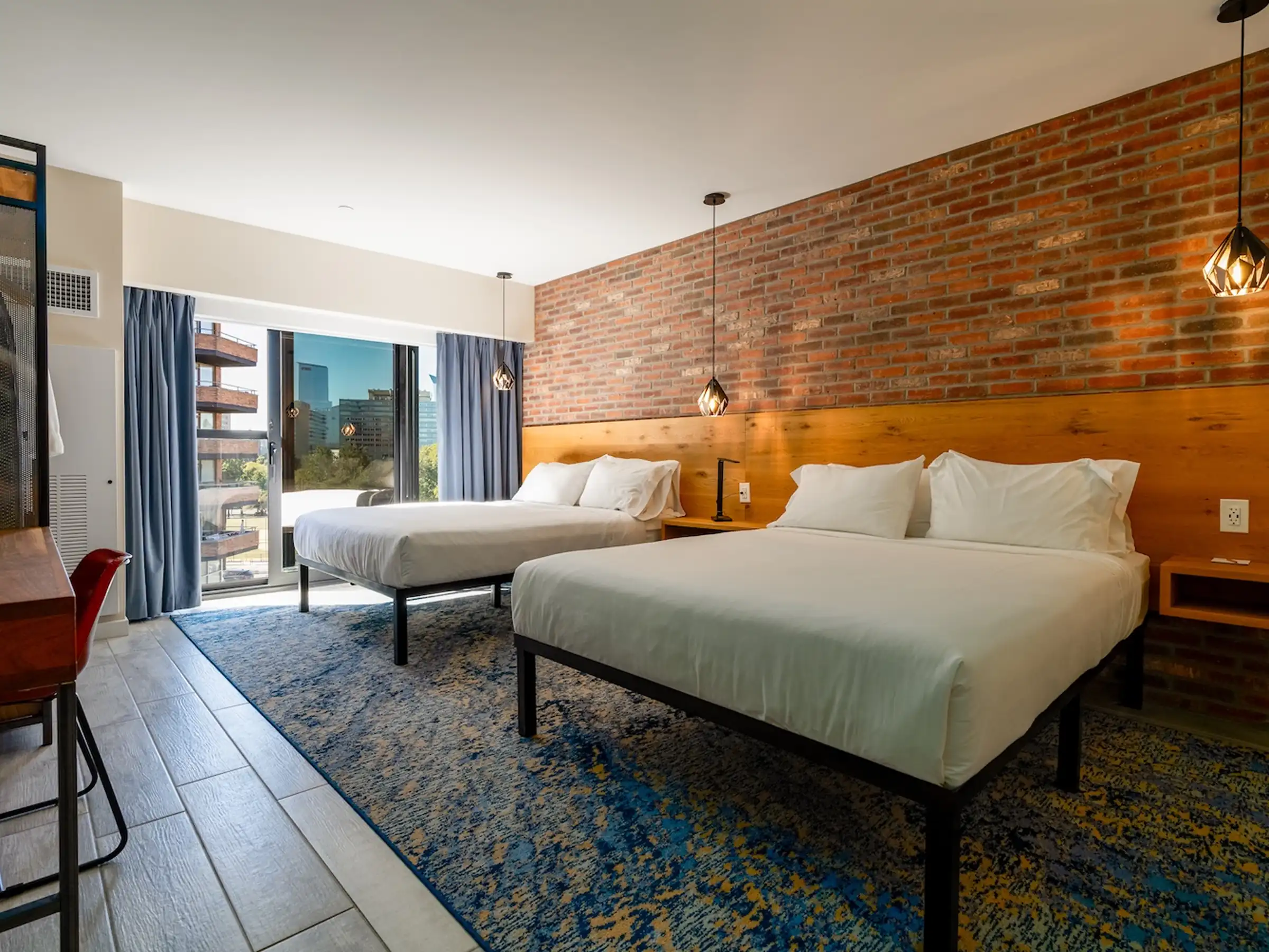 Porcelain tile flooring with a blue patterned area rug in a boutique hotel guest room with exposed brick wall and private balcony.