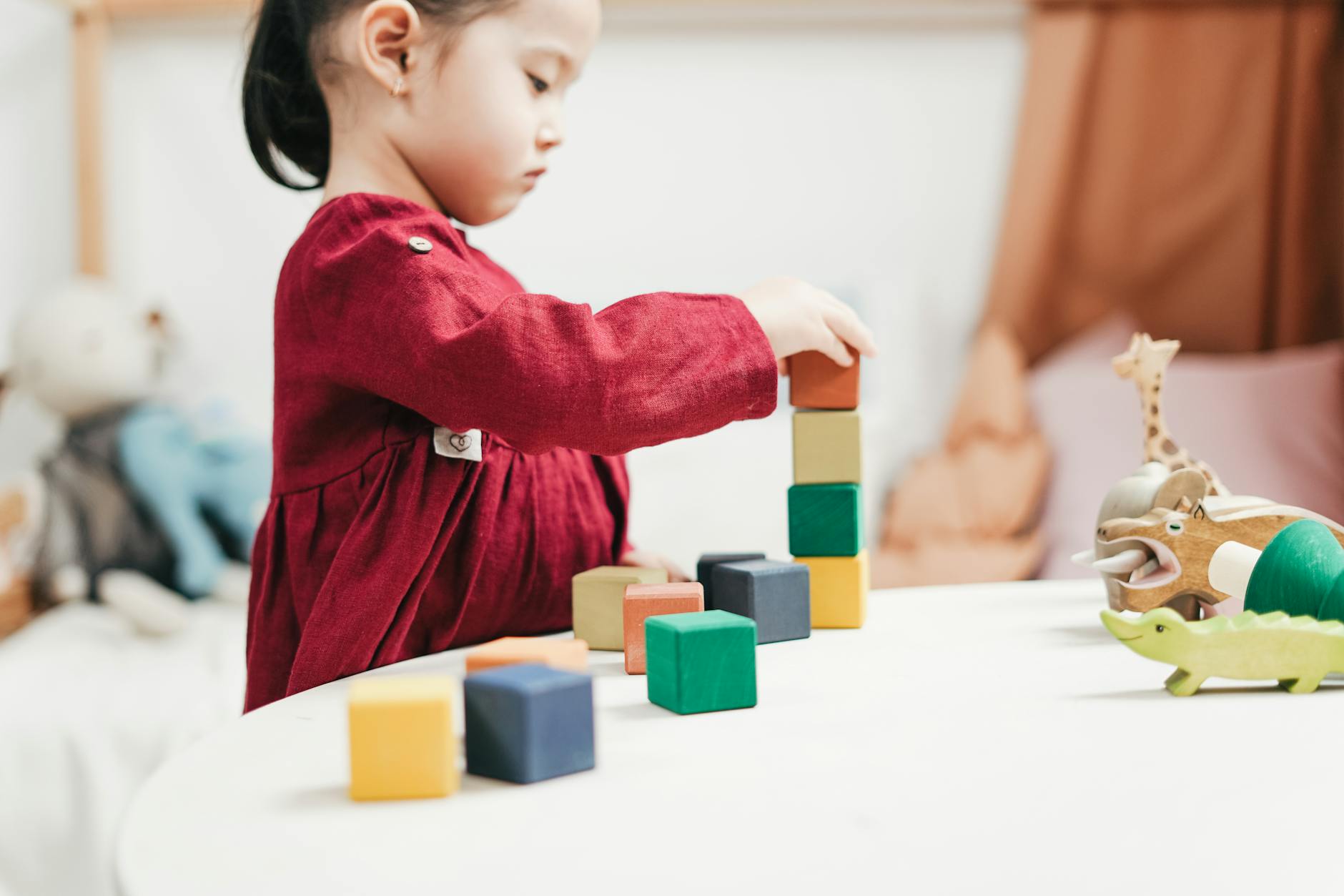 A smiling young child building a tall tower with colorful wooden blocks on a classroom rug.