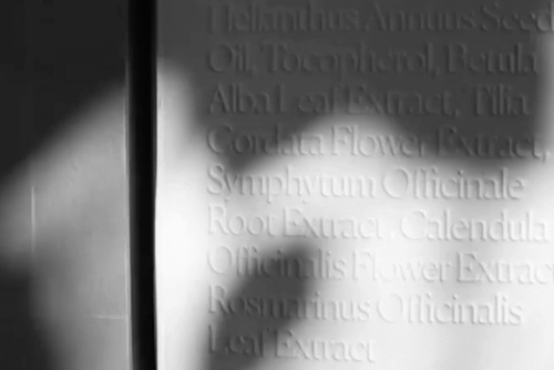 A monochrome macro animation captures a play of light and shadow across a Krayna product box, revealing deeply embossed botanical names. This high-end packaging design highlight emphasizes the tactile, premium nature of the sustainable brand identity created for the vegan skincare line.