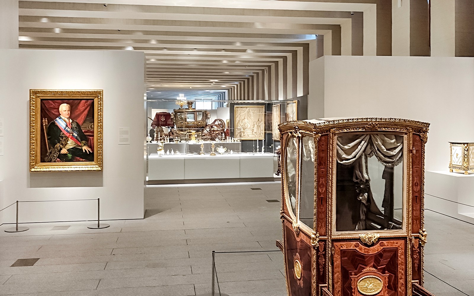 Royal Collections Gallery in Madrid featuring a historic carriage and portrait.