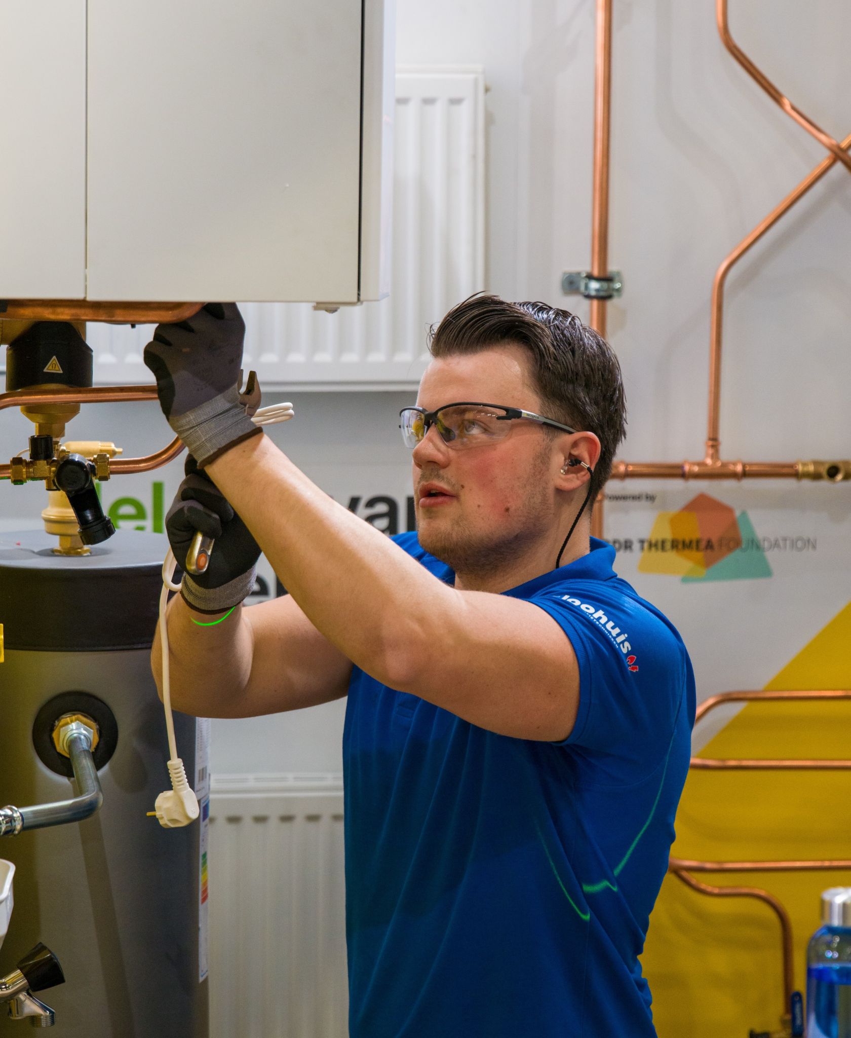 Young male technician in safety glasses and gloves connecting wiring on a boiler at a BDR Thermea Foundation skills competition