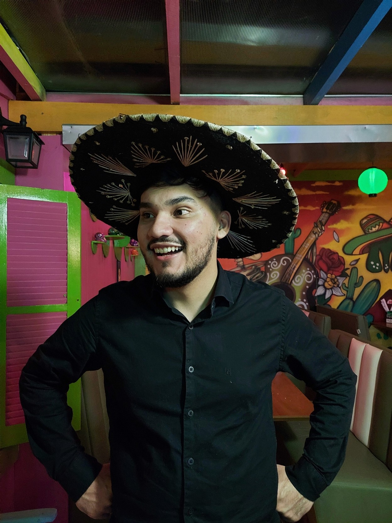 Pessoa sorrindo em ambiente interno colorido, usando chapéu mexicano tradicional