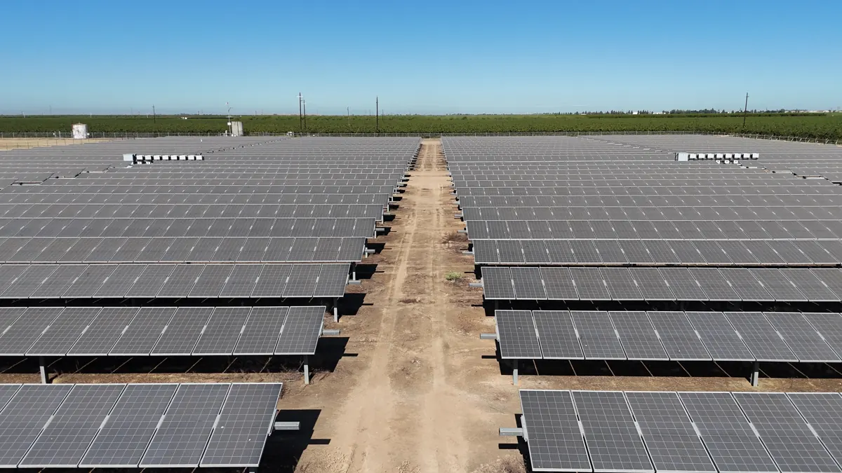 Drone view down a dirt lane between ground-mount solar arrays at Wine Group in Madera County, CA