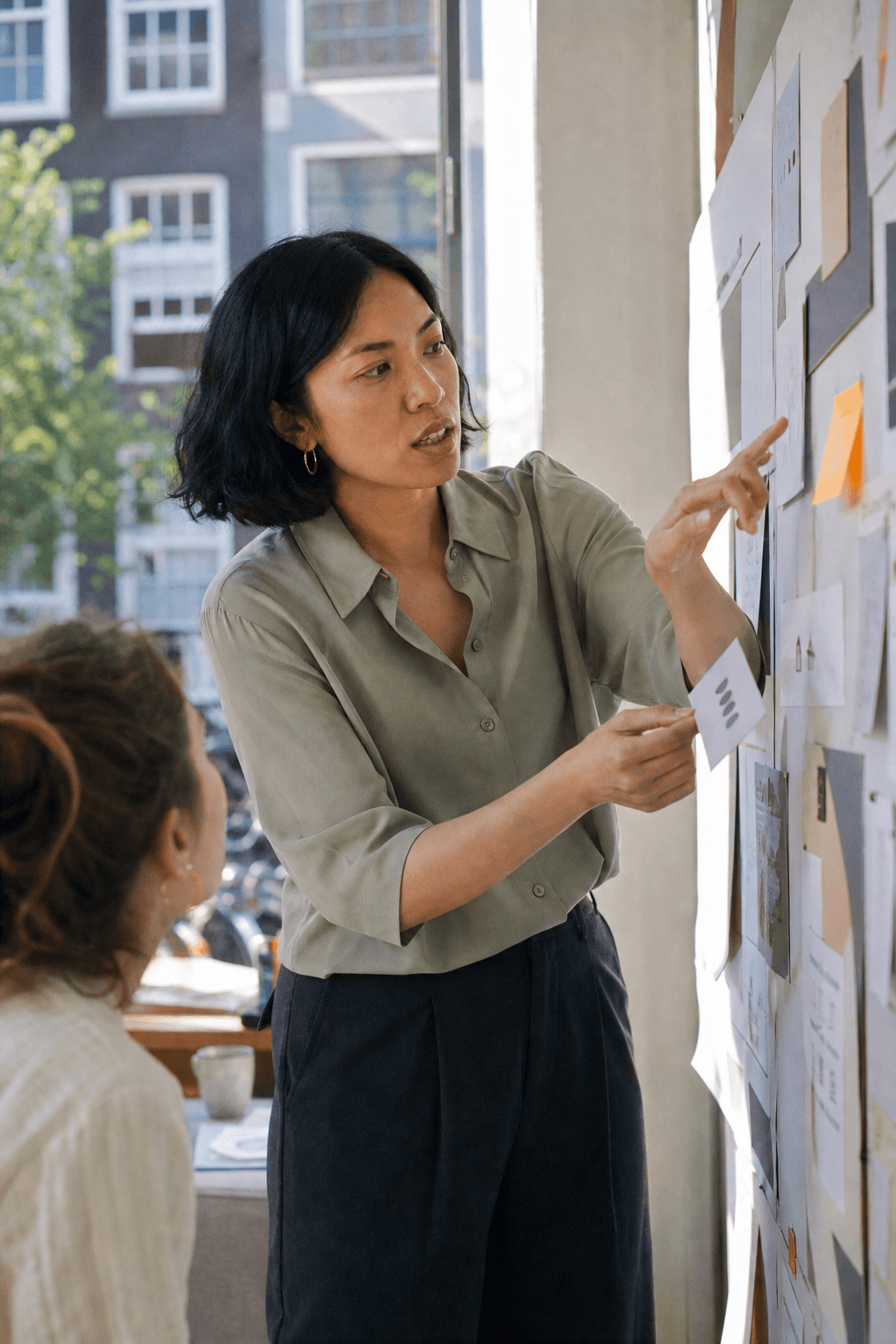 Discussing a printed presentation board with a colleague, pointing to a card with unreadable placeholder marks.