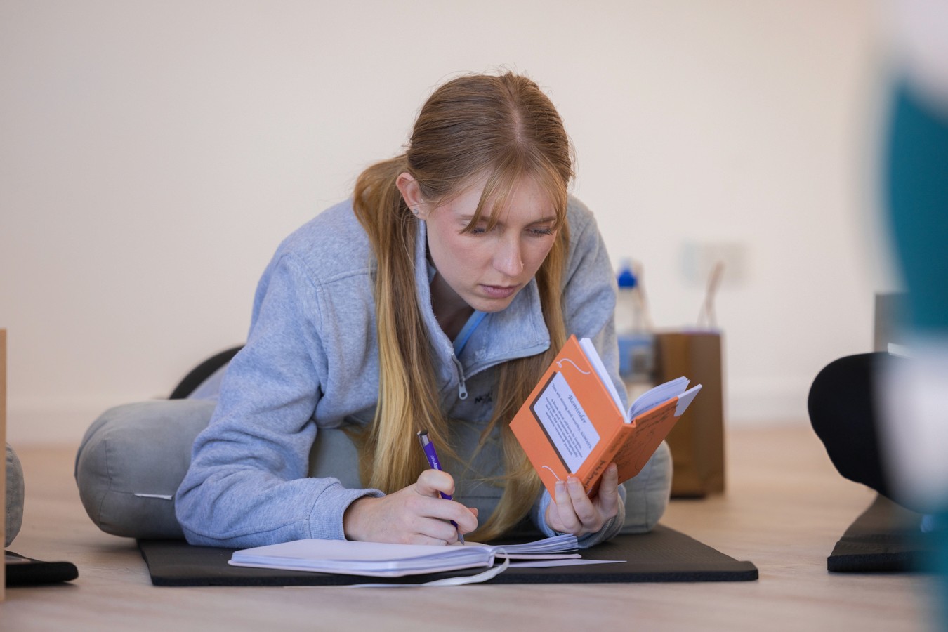Woman sitting cross legged on the floor leaning forward, writing into a book