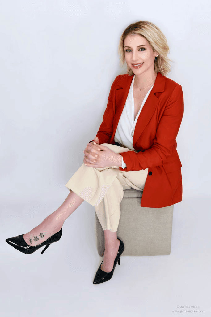 Woman in red blazer and cream pants sitting.