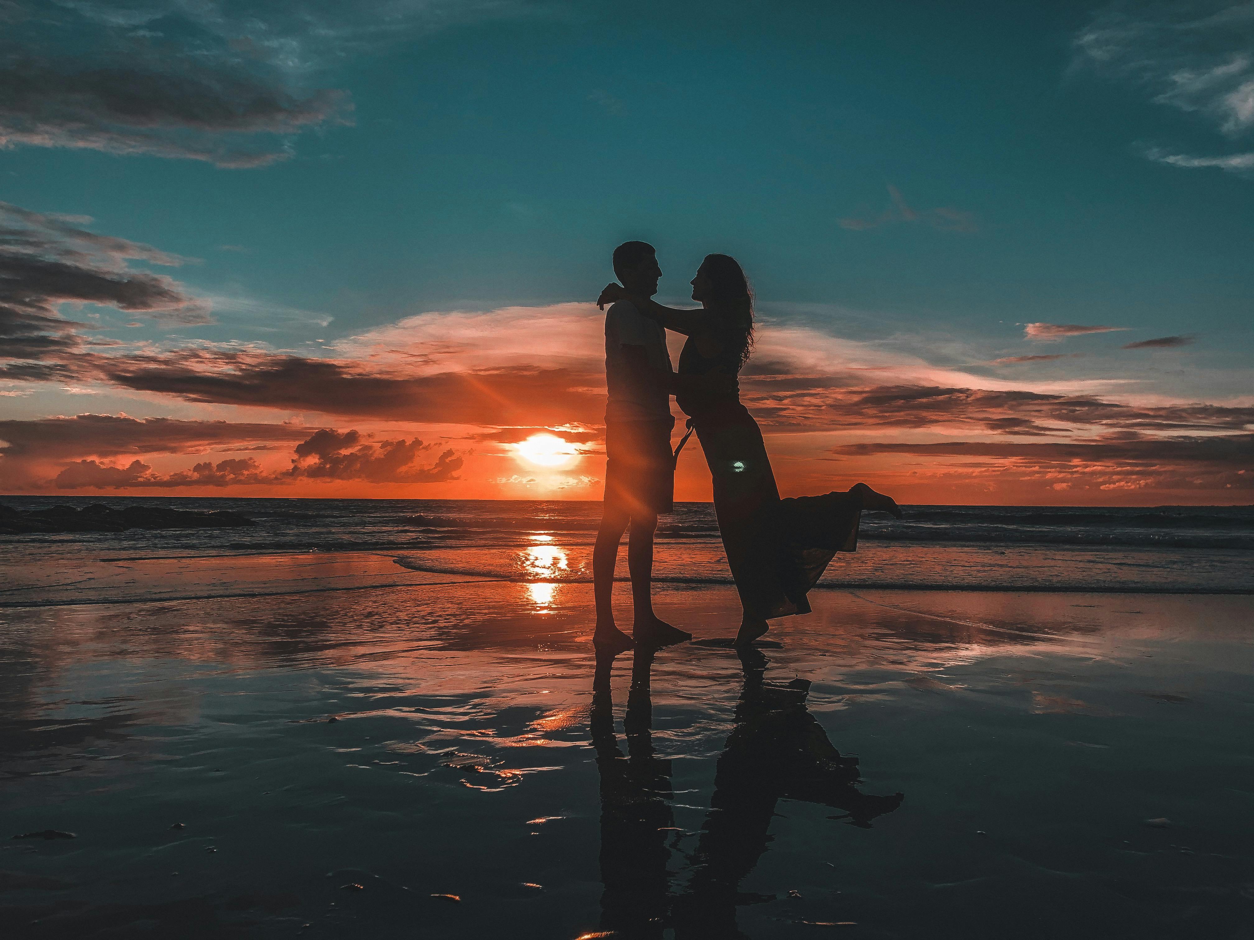 ilhouette of a couple embracing on a Bali beach during a breathtaking sunset, symbolizing love and tranquility.