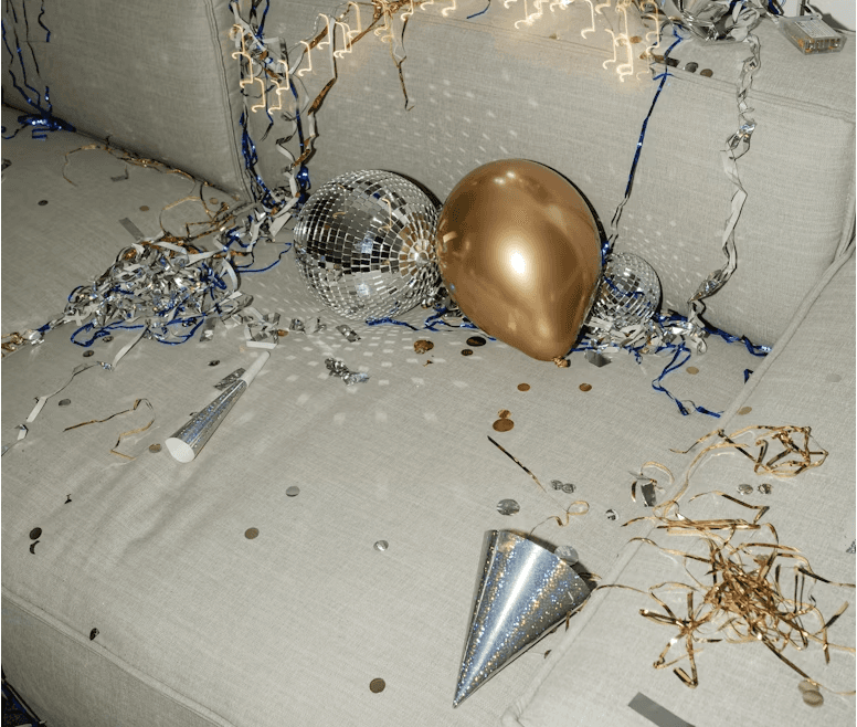 After-party scene with balloons, streamers, and two people lounging on a messy couch in a small apartment.