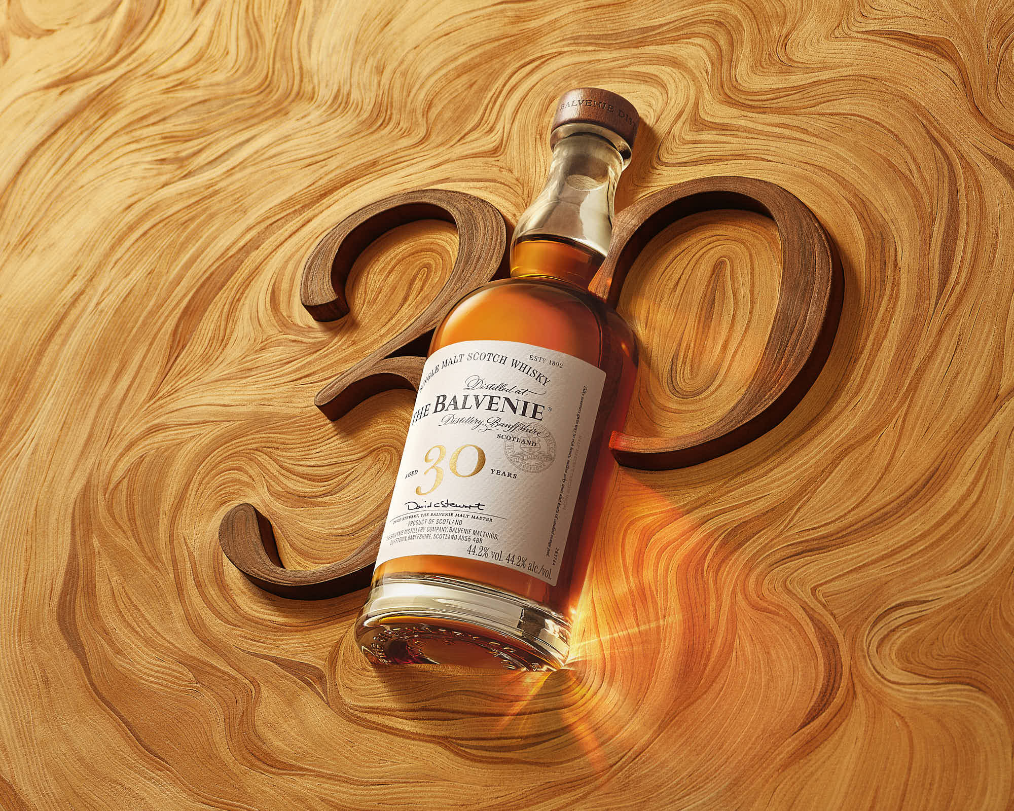 A bottle of whiskey rests on a wooden surface with the number 30 elegantly placed beside it.