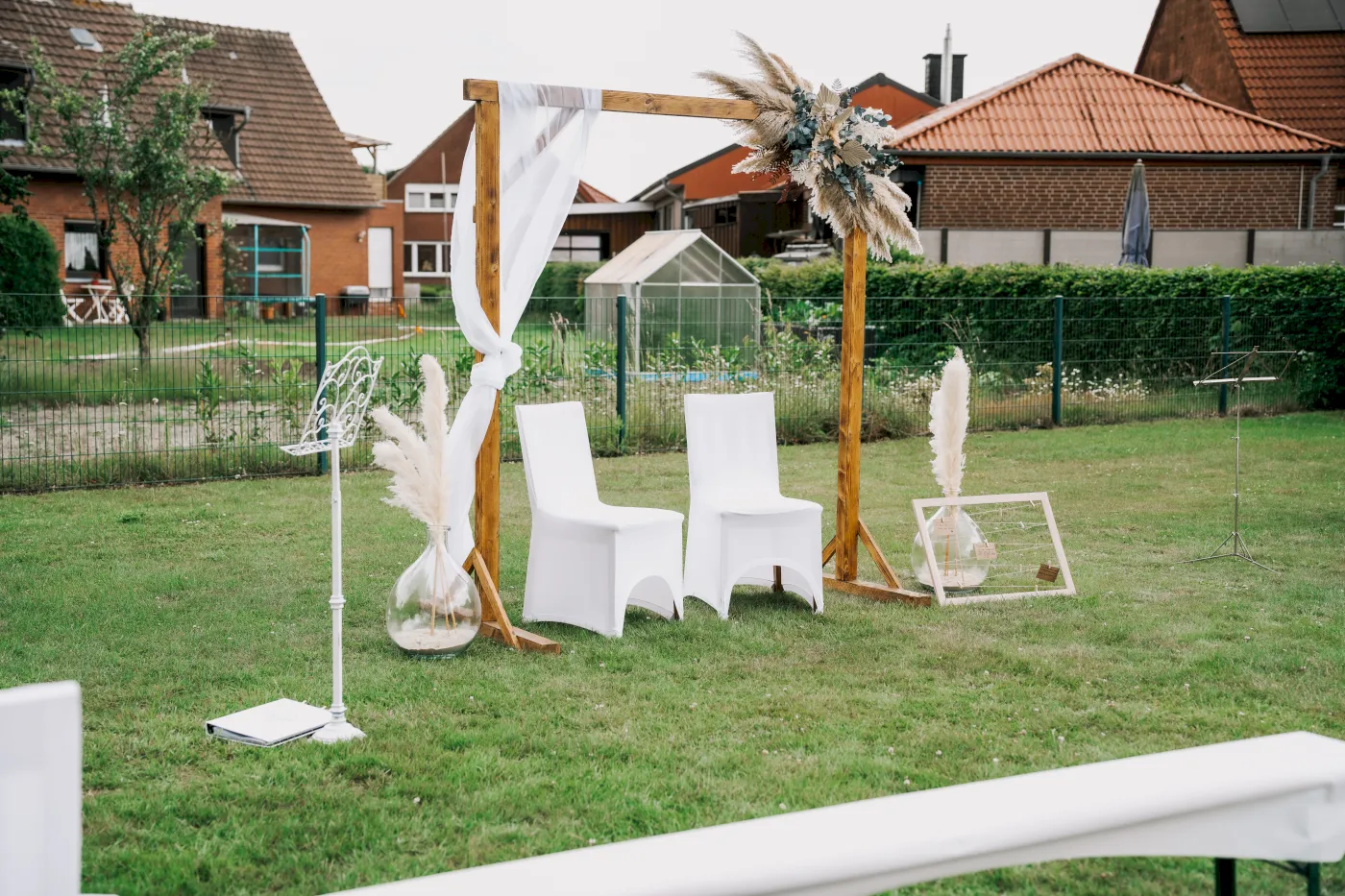 Hochzeit im Freien: Holzrahmen, weiße Stühle und Dekoration für eine Zeremonie. Romantisches Ambiente.