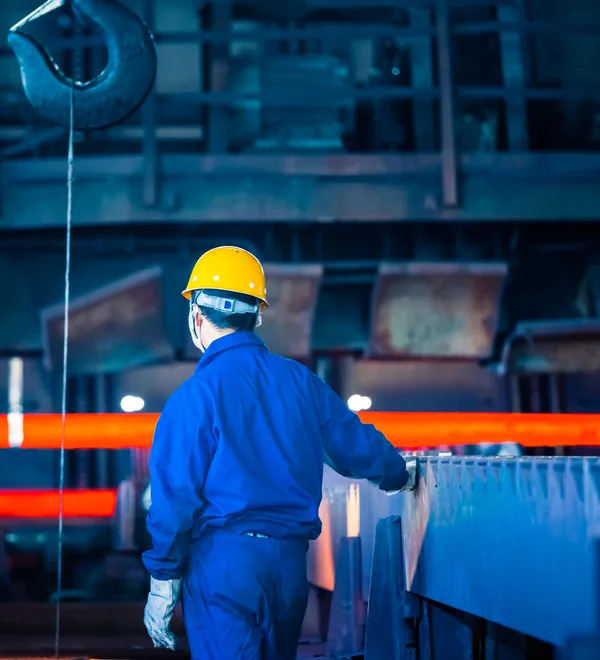 Steel plant worker in a hard hat watching the hot rolling line from the mill floor
