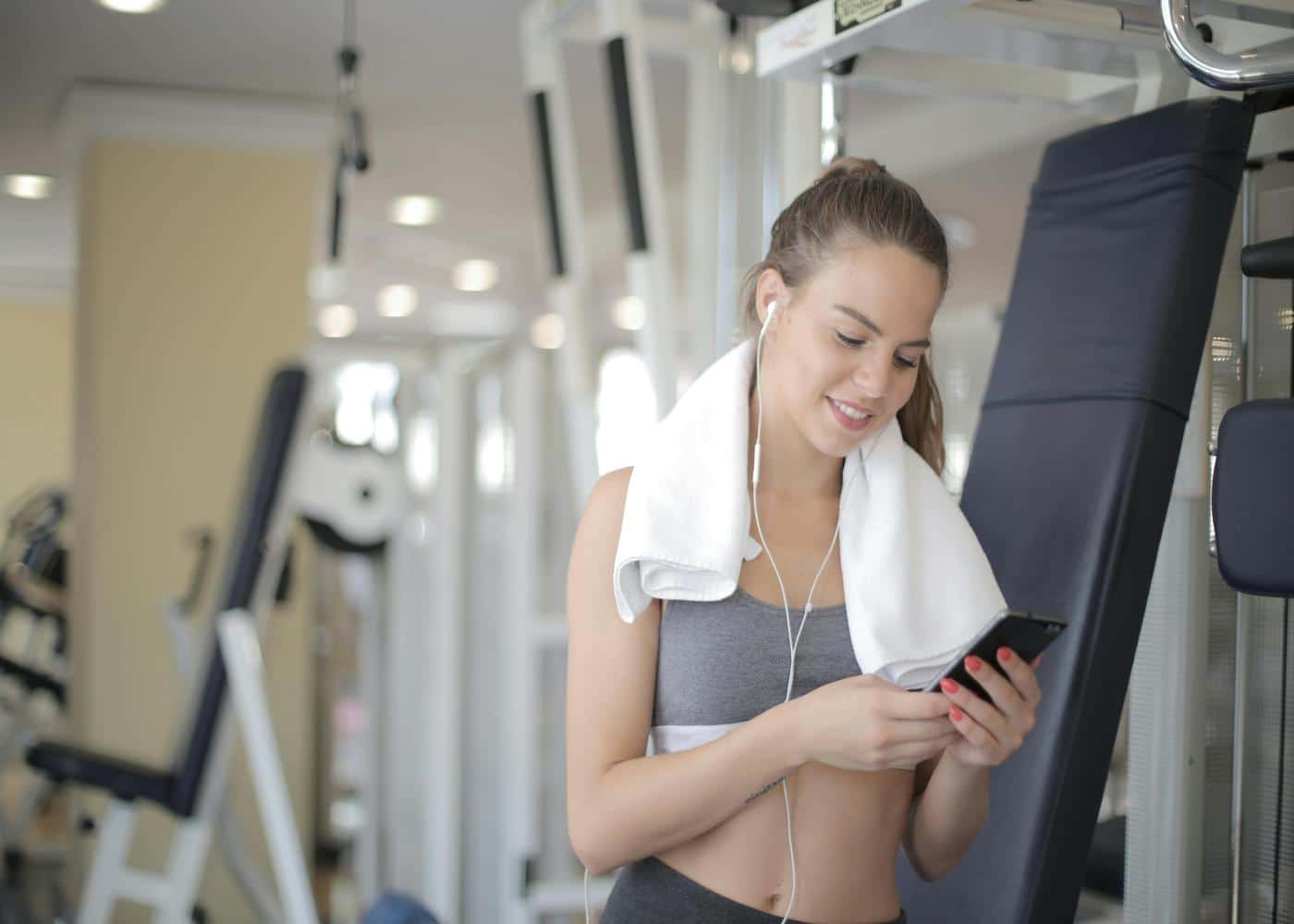 Woman at gym with towel around neck looking at smartphone