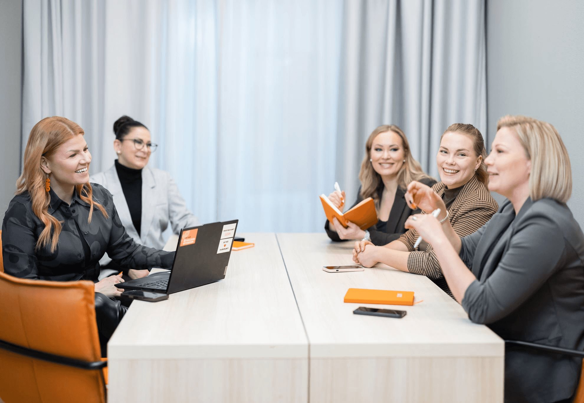 Viisi Network & Growthin valmentajaa keskustelee pöydän ääressä; läppäri, muistiot ja kahvit – taustalla vaalea verho.