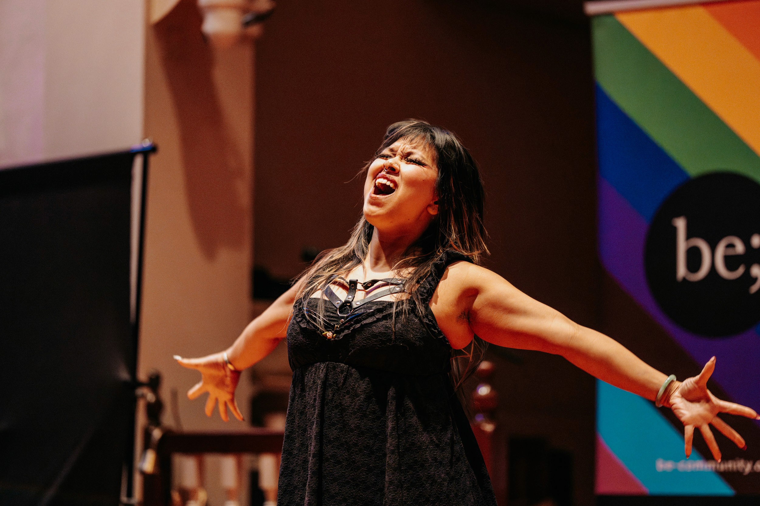 Performer singing passionately on stage at Queer Open Mic hosted by be; community in Bridgewater, Massachusetts
