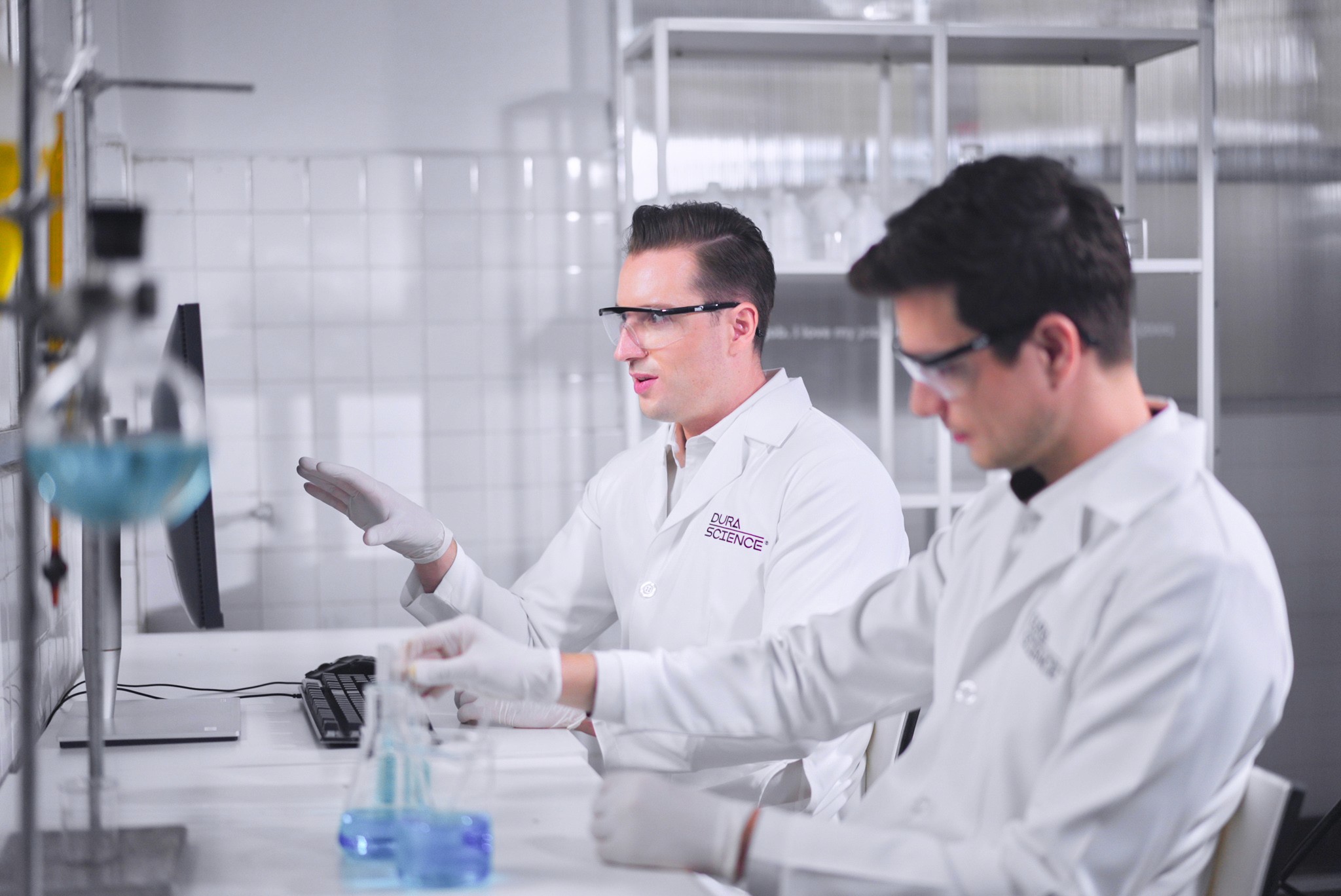 Close-up portrait of a person wearing a gray insulated hooded jacket with the hood up, showing their face framed by the hood against a light background.