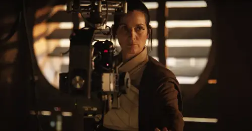 Carrie Anne Moss in a white and brown robe in front of a film camera