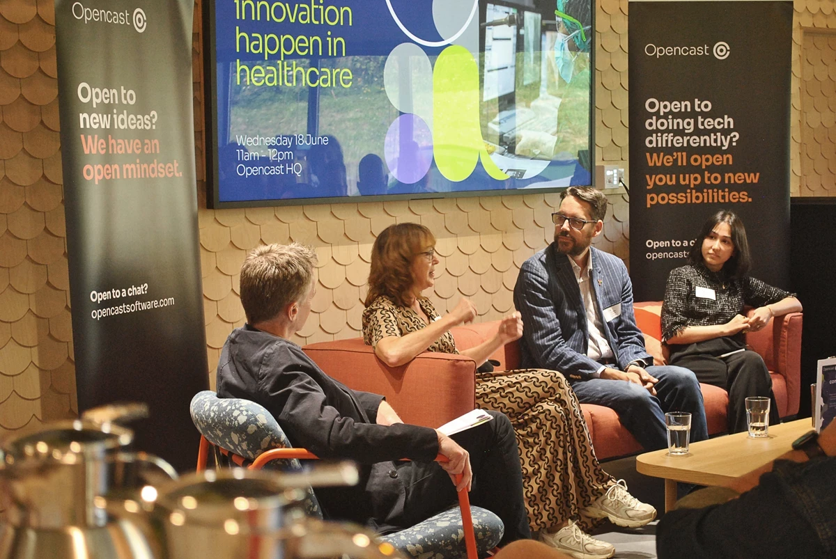 a group of four people sitting on a sofa and chairs sit in front of a screen in a room full of people