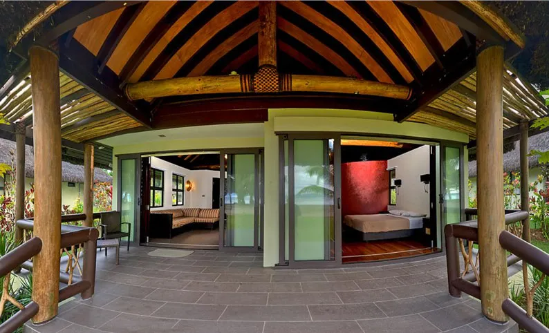 Covered patio entry to an Uprising Beach Resort bure, revealing a living room and bedroom with ocean view.