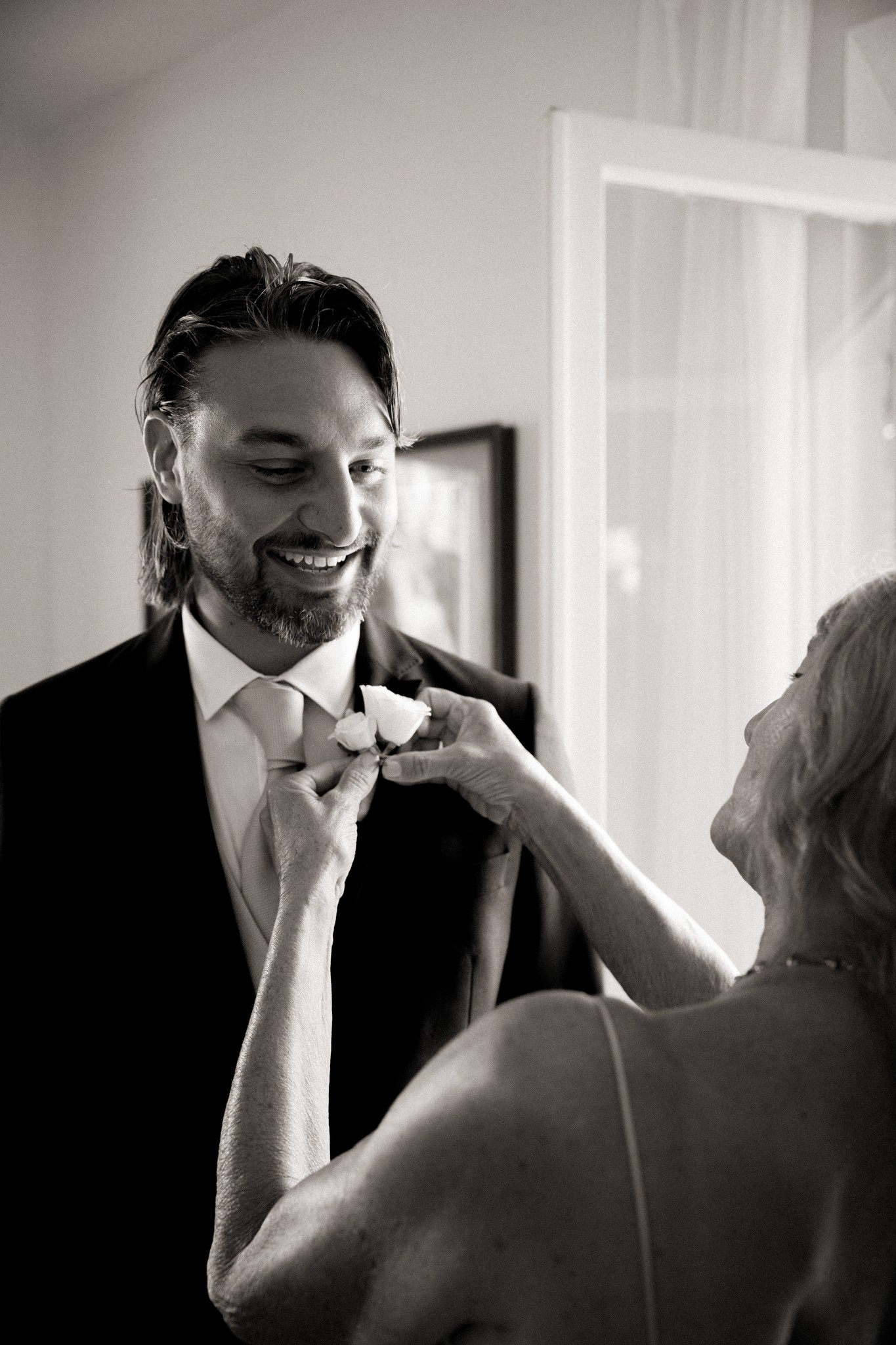 Lucio sorride mentre la madre sistema la farfallina durante i preparativi del matrimonio a Bolgheri