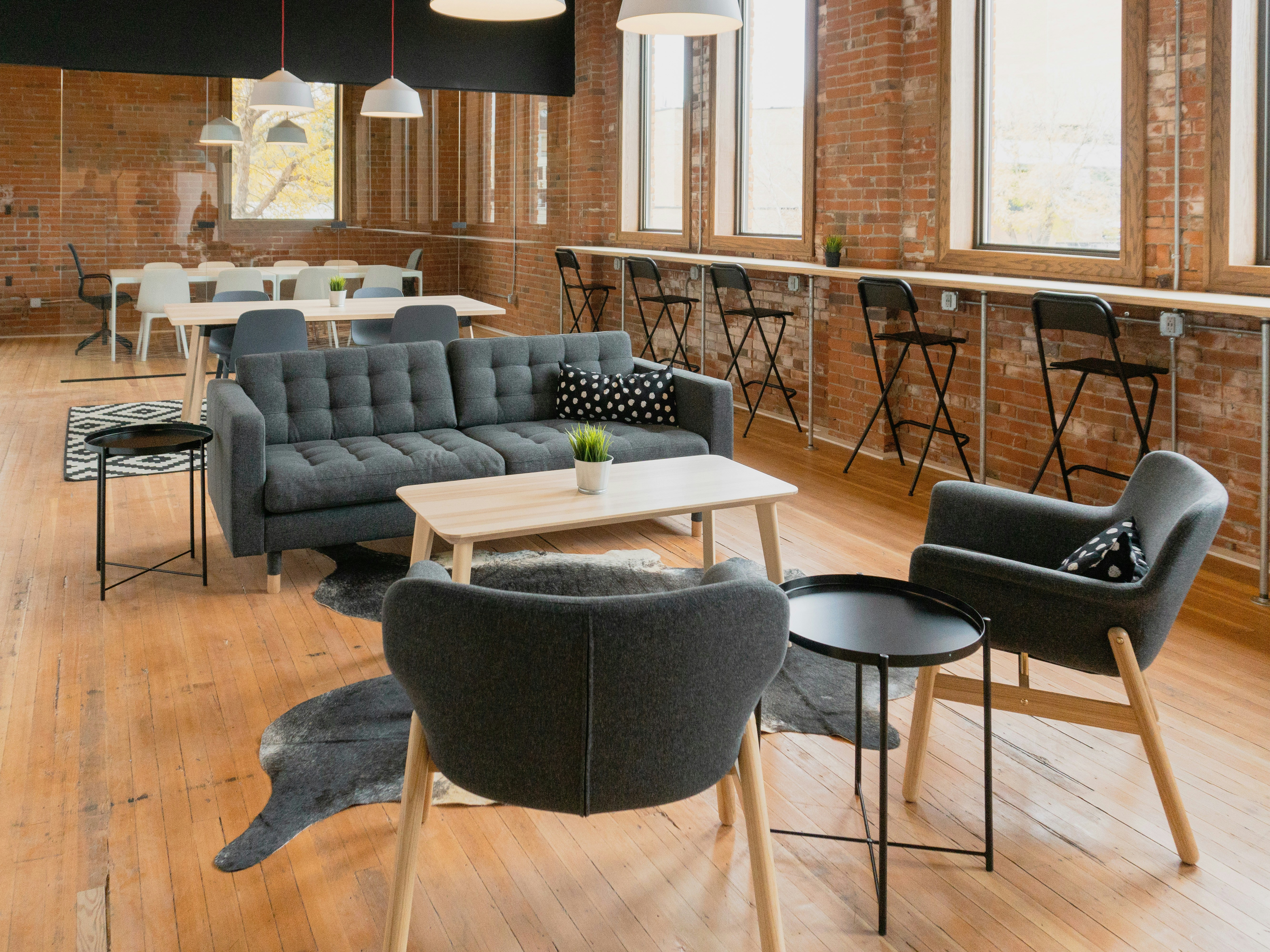 Industrial coworking lounge with exposed brick, charcoal sofas, and warm hardwood floors