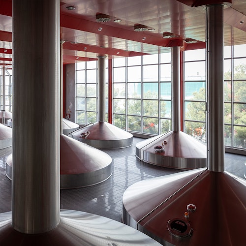 工业房间内设有大型银色圆锥形罐、红色天花板以及展示外面绿意的落地窗。