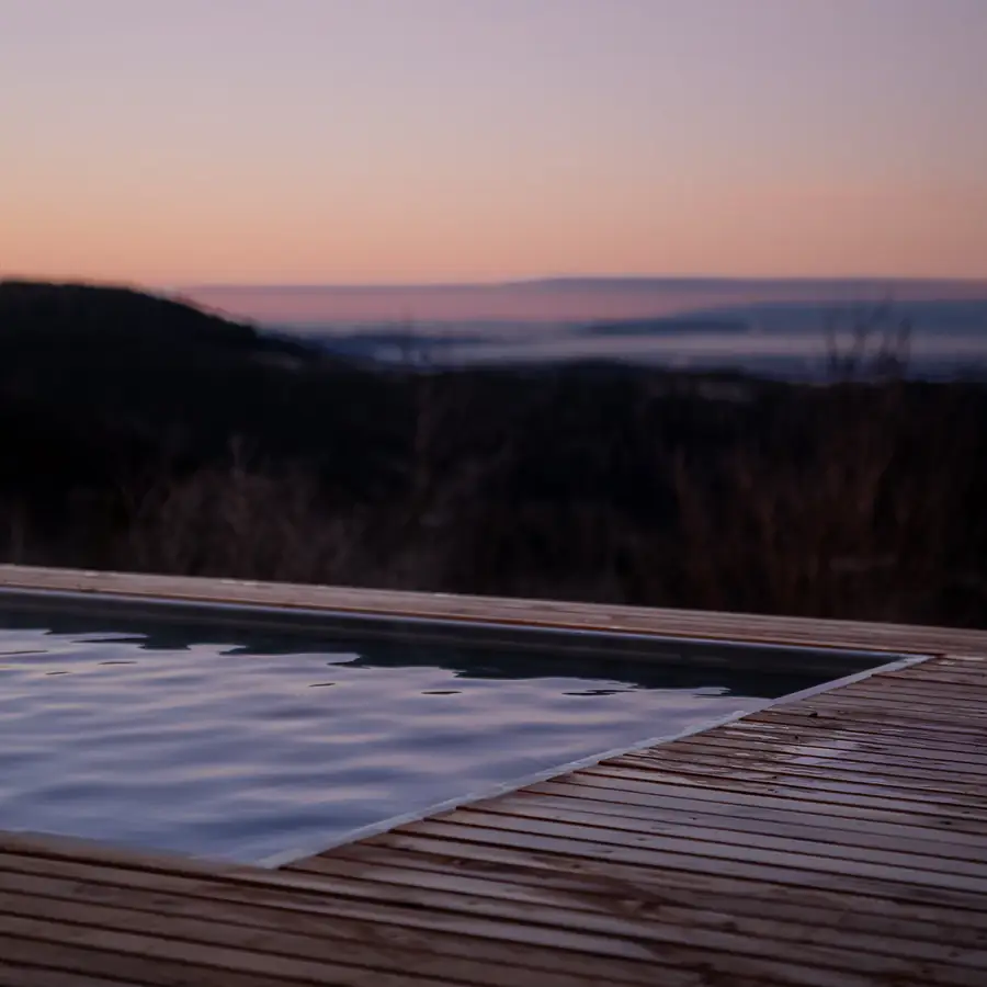 Beheizter Pool auf dem Holzdeck vor rosa gefärbtem Morgenhimmel