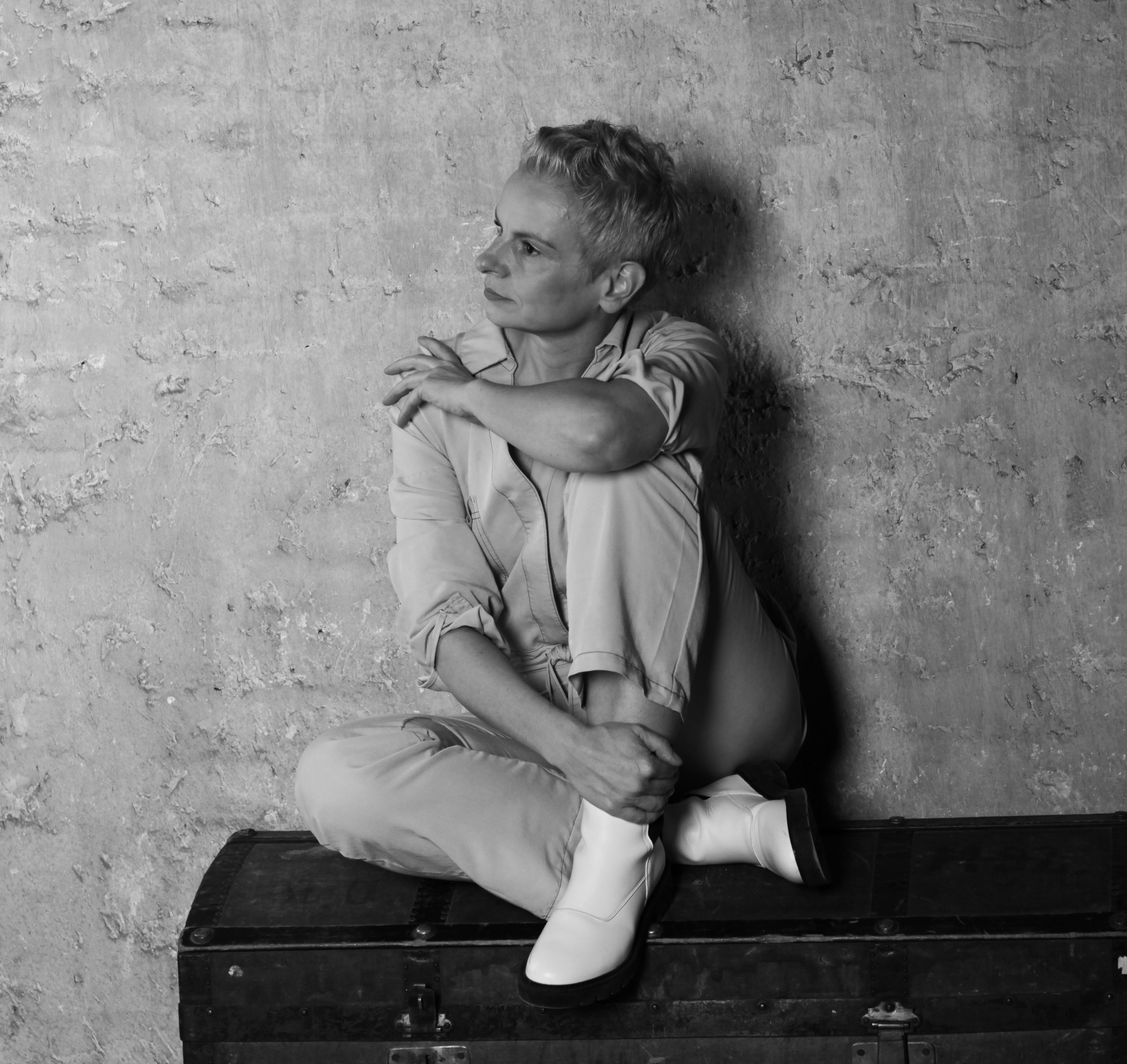 A thoughtful young person with dark hair gazes to the side, captured in soft black and white lighting.