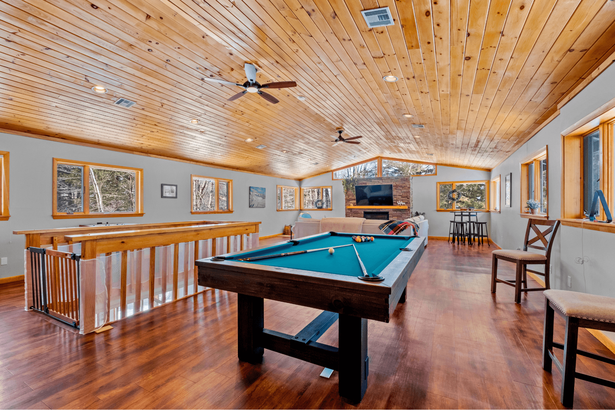 Spacious upstairs game room featuring a full-size pool table, wood-paneled ceiling, and large windows, ideal for guests of all ages at this top-rated New Hampshire short-term rental.