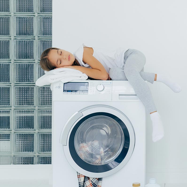 Пральна машина з фронтальним завантаженням у світлій ванній кімнаті, дитина відпочиває зверху