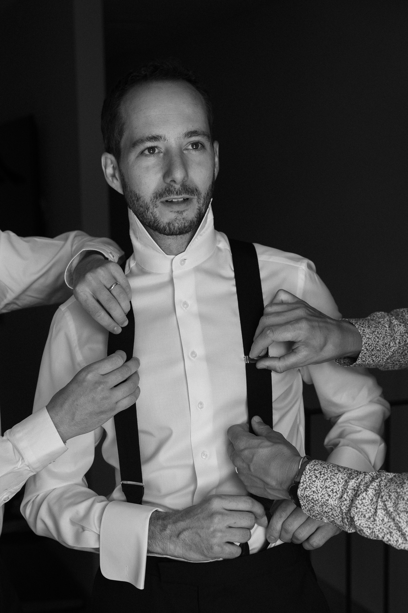Sposo in camicia bianca e bretelle si prepara mentre gli amici aggiustano la cravatta, reportage matrimoniale
