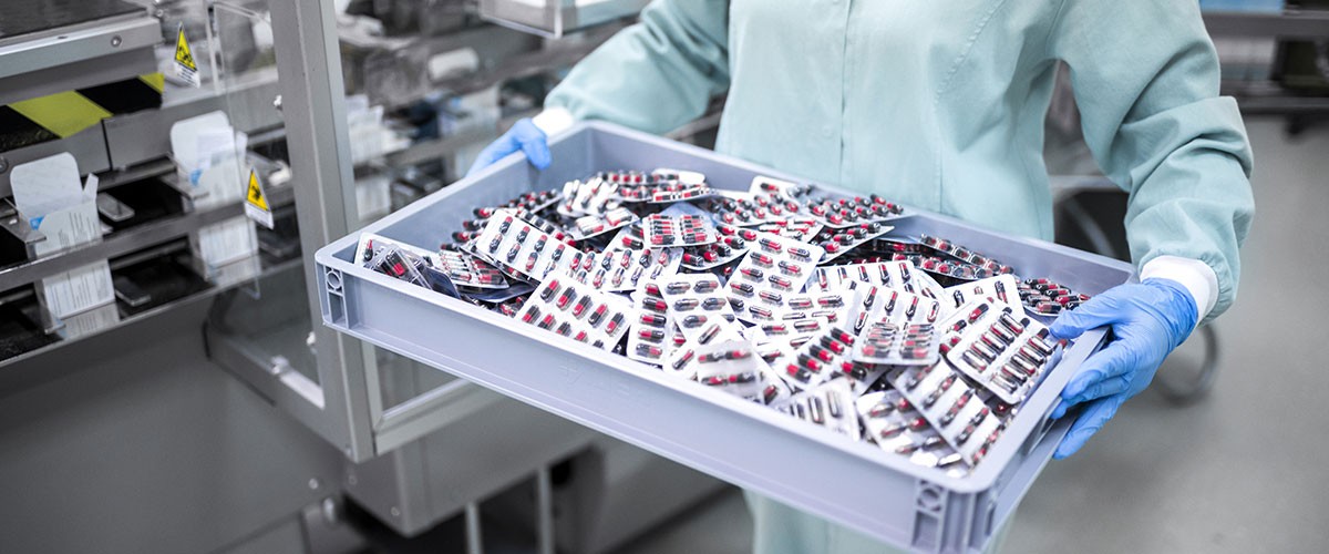 A person in protective gear holds a tray filled with various items in a laboratory or industrial setting.