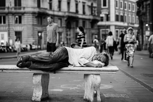 A person lying on a street bench sleeping.