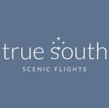 A young man with light brown hair is wearing a black suit jacket and white shirt, standing in a softly lit office setting, conveying professionalism.