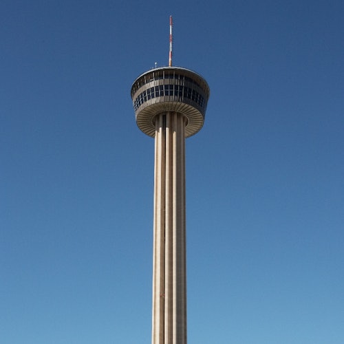 A tall observation tower with a circular observation deck and antenna on top, set against a clear blue sky.