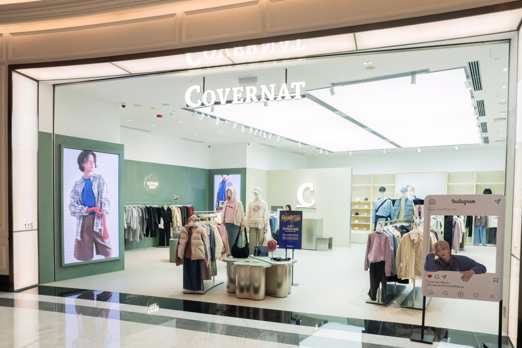 The storefront of the clothing store 'Covenat', featuring a large display of apparel, a promotional sign, and digital screens showcasing models wearing the clothes.