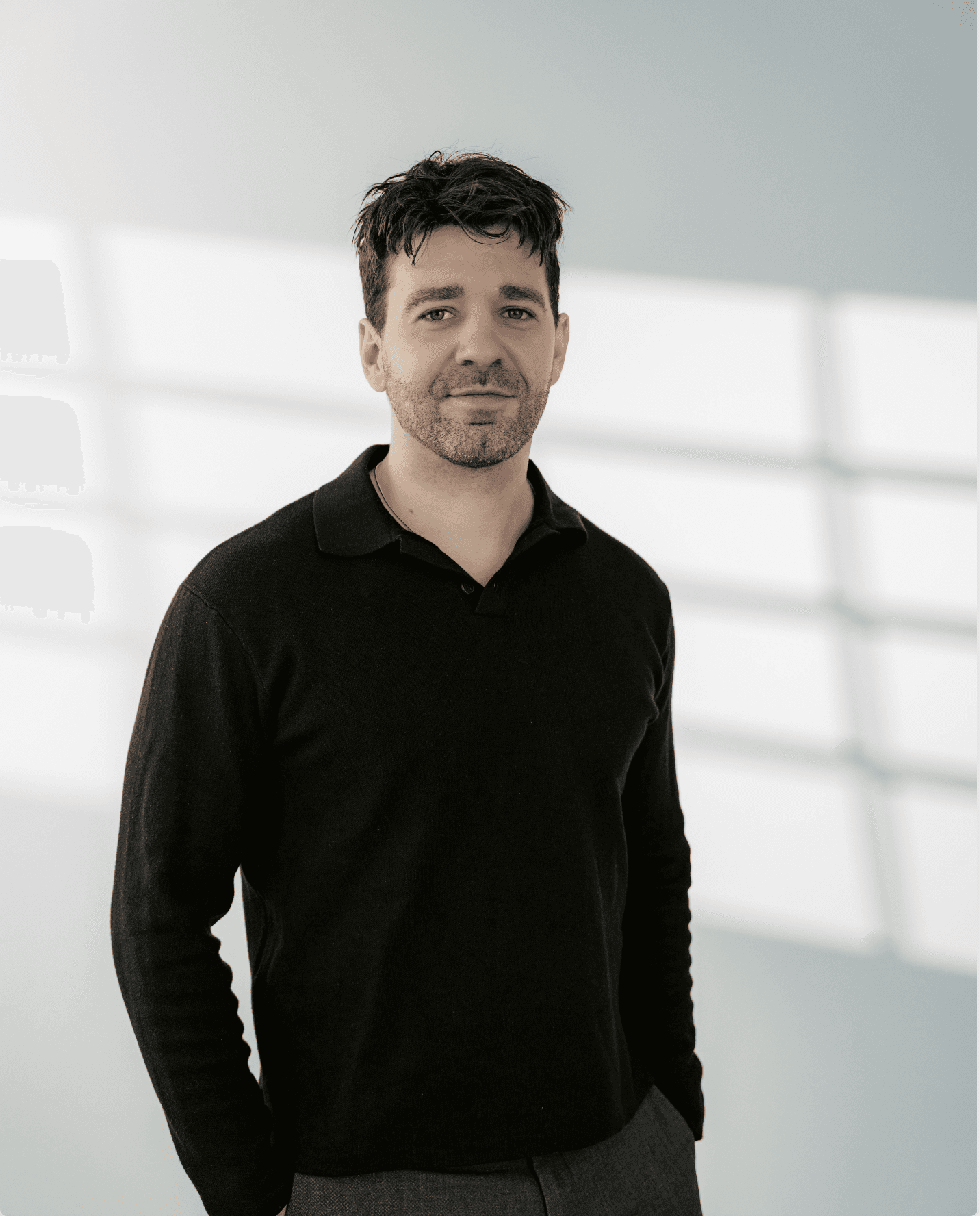 Ein Junger Mann mit schwarzem Pulllover und Hände in der Tasche blickt freundlich in die Kamera.