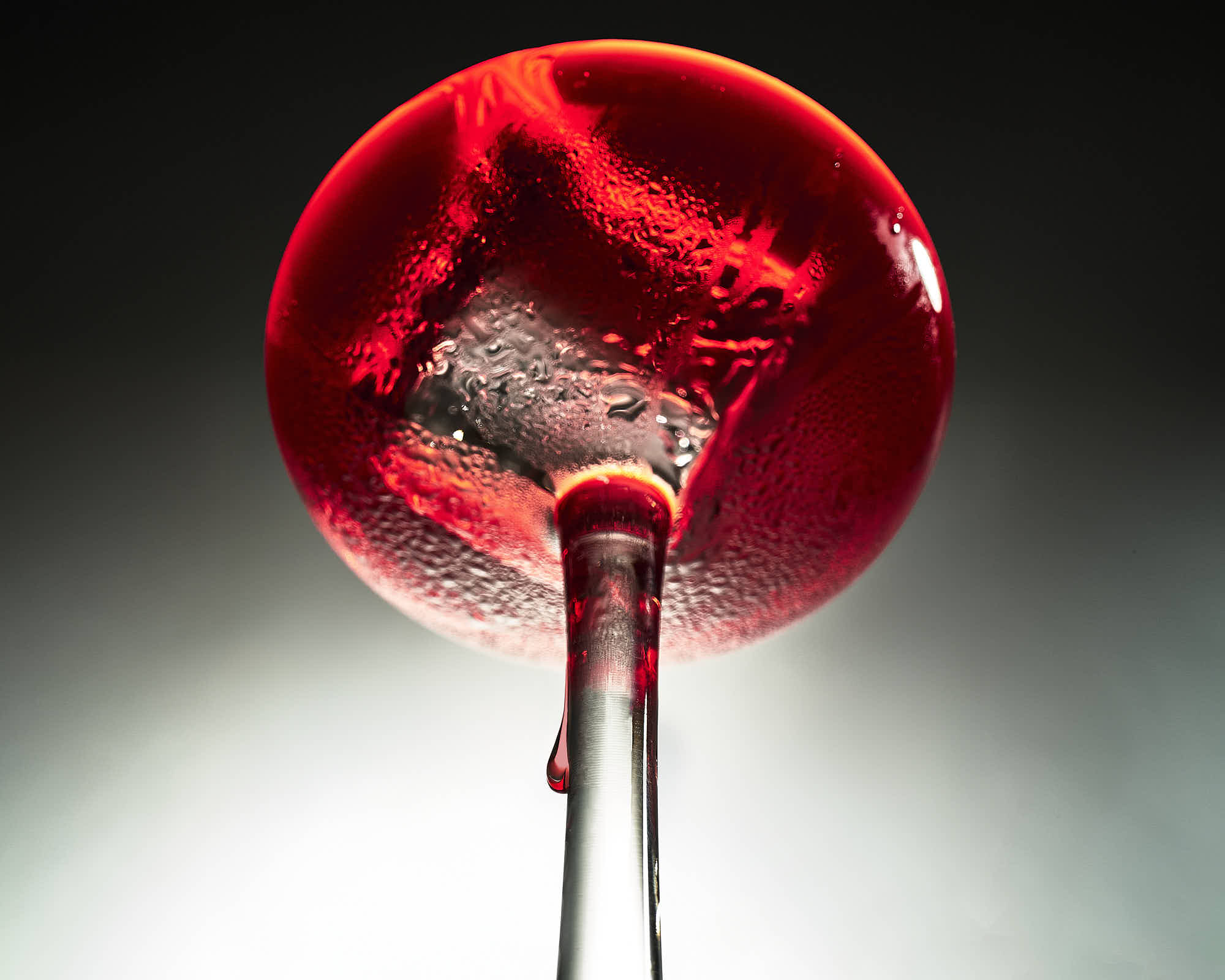 Close-up of red liquid in a glass with textured surface and dramatic lighting.