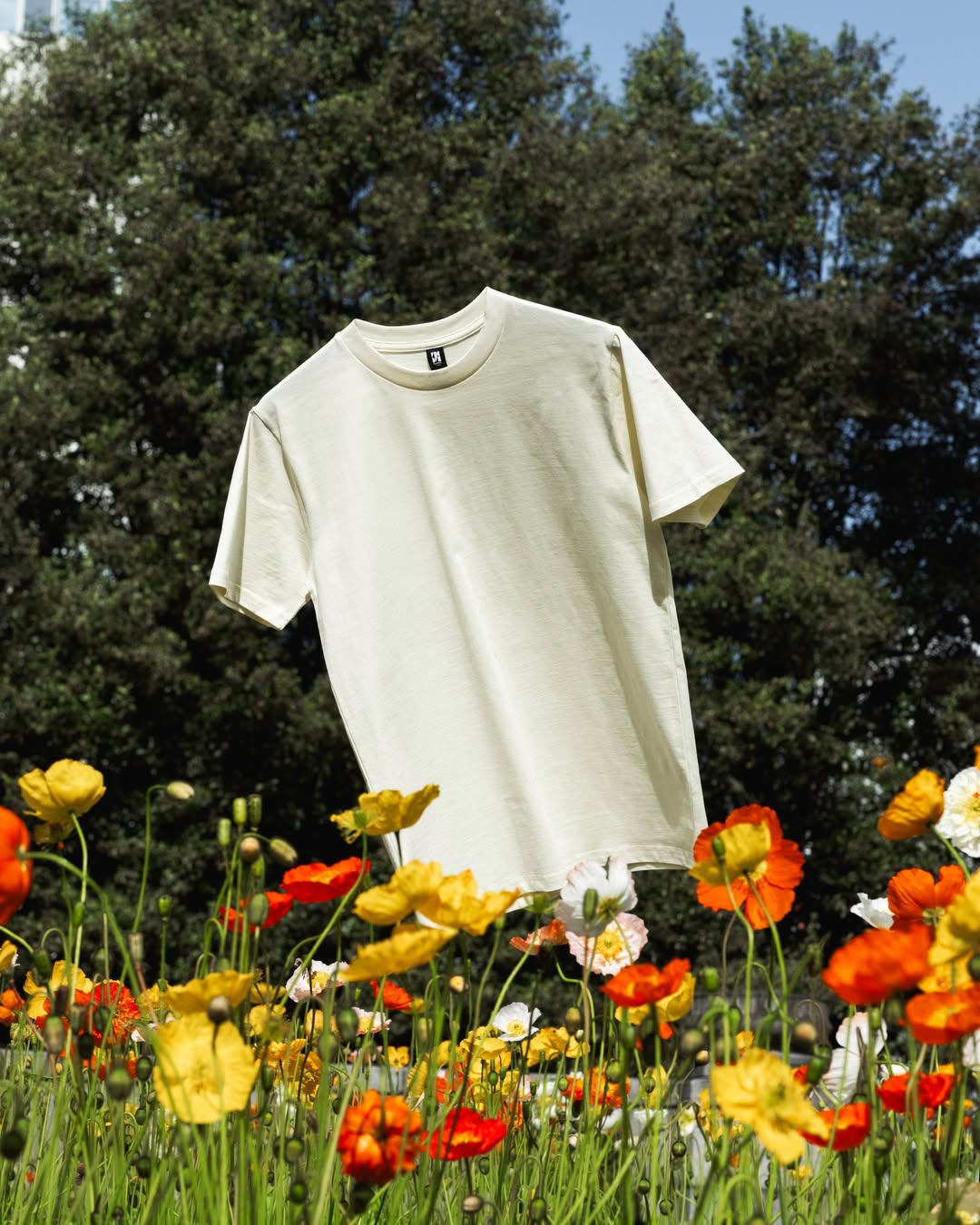 A shirt that looks like its free flating in a field of poppies in the forest that has pine trees in the background.