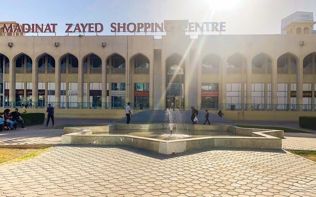 The sun shines brightly on the front of Al Forsan Village shopping centre, highlighting its modern architecture.