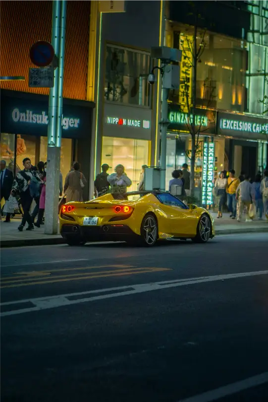 Rear view of a yellow Ferrari convertible parked on an urban street at night with glowing taillights