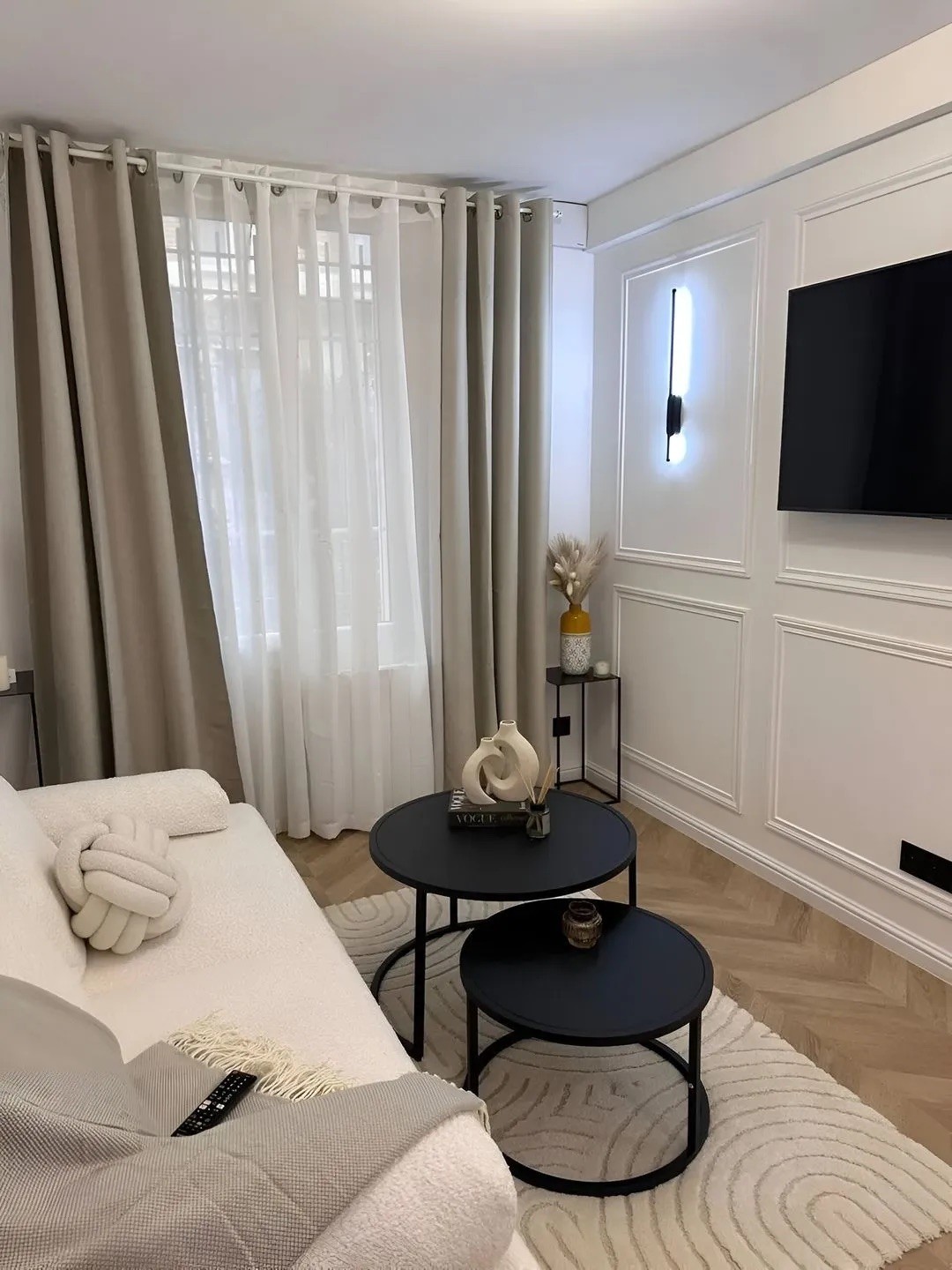 Aménagement d'un micro-studio de 14 m² à Paris avec canapé blanc, moulures murales classiques et TV encastrée.