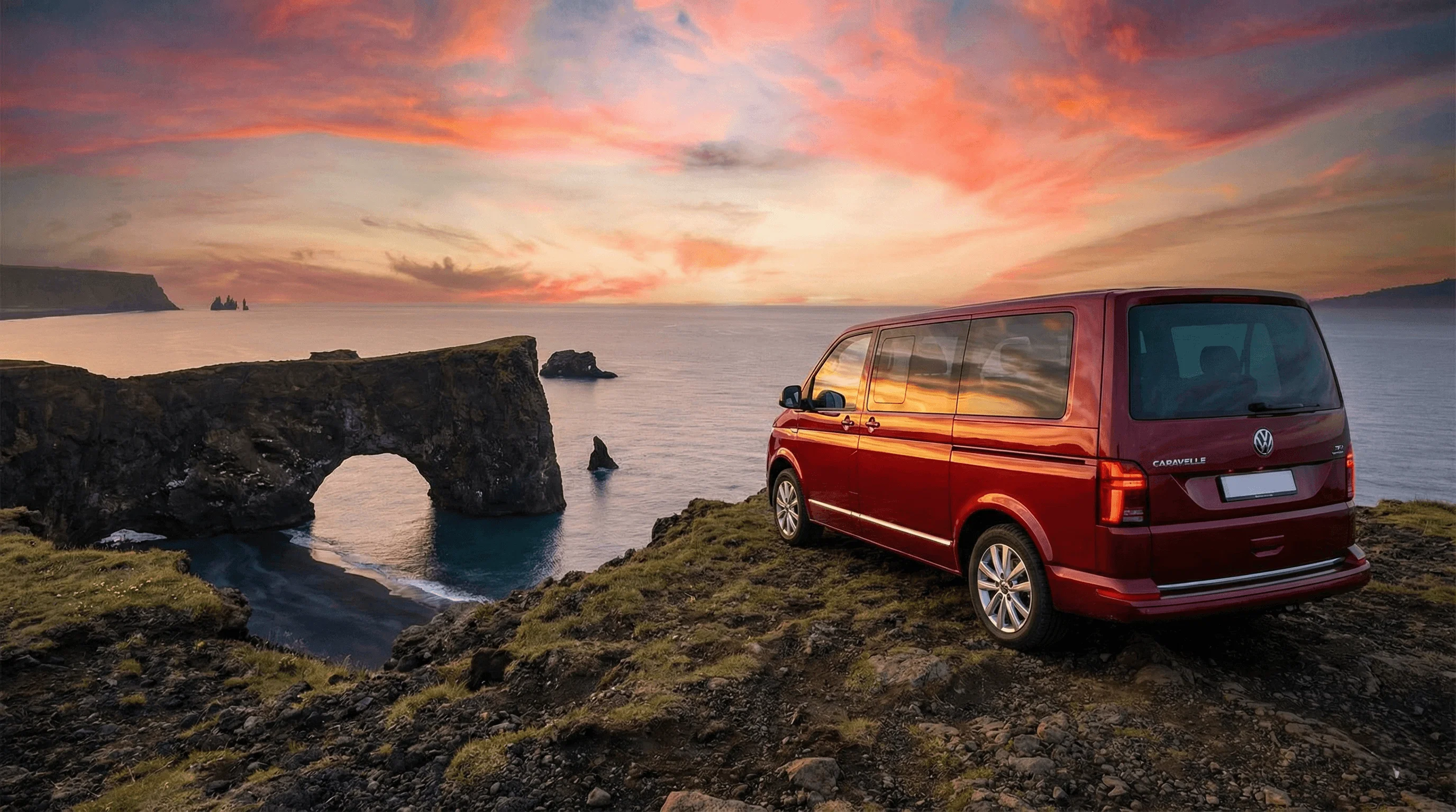 A red camper van parked on a cliff edge overlooking the ocean and a natural stone arch at sunset.