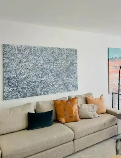 Modern living room featuring a grey sofa with colorful pillows and large abstract wall art.