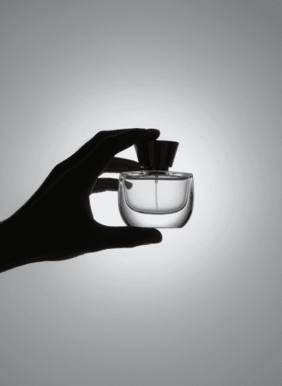 A silhouetted hand delicately holds a round perfume bottle against a gradient gray background, conveying elegance and simplicity.