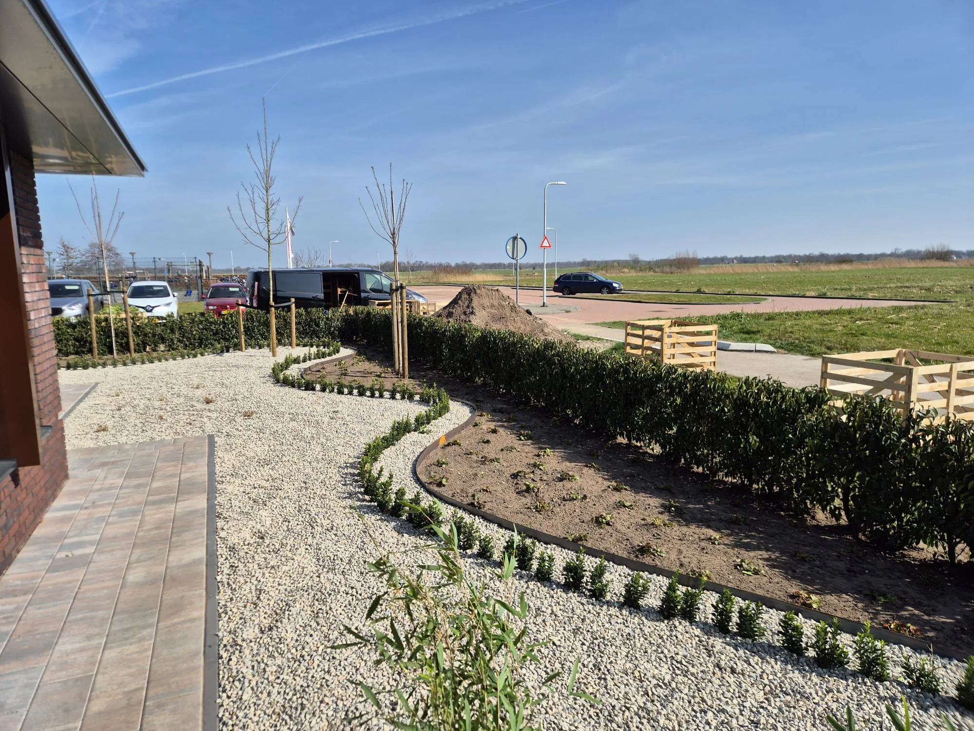 Nieuw aangelegde Japanse tuin met grind, jonge bomen, lage heggen en een open zicht op het Friese landschap bij nieuwbouwwoning.