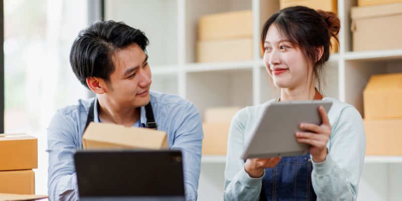 Two retail staff manage inventory and orders using a tablet and laptop. 