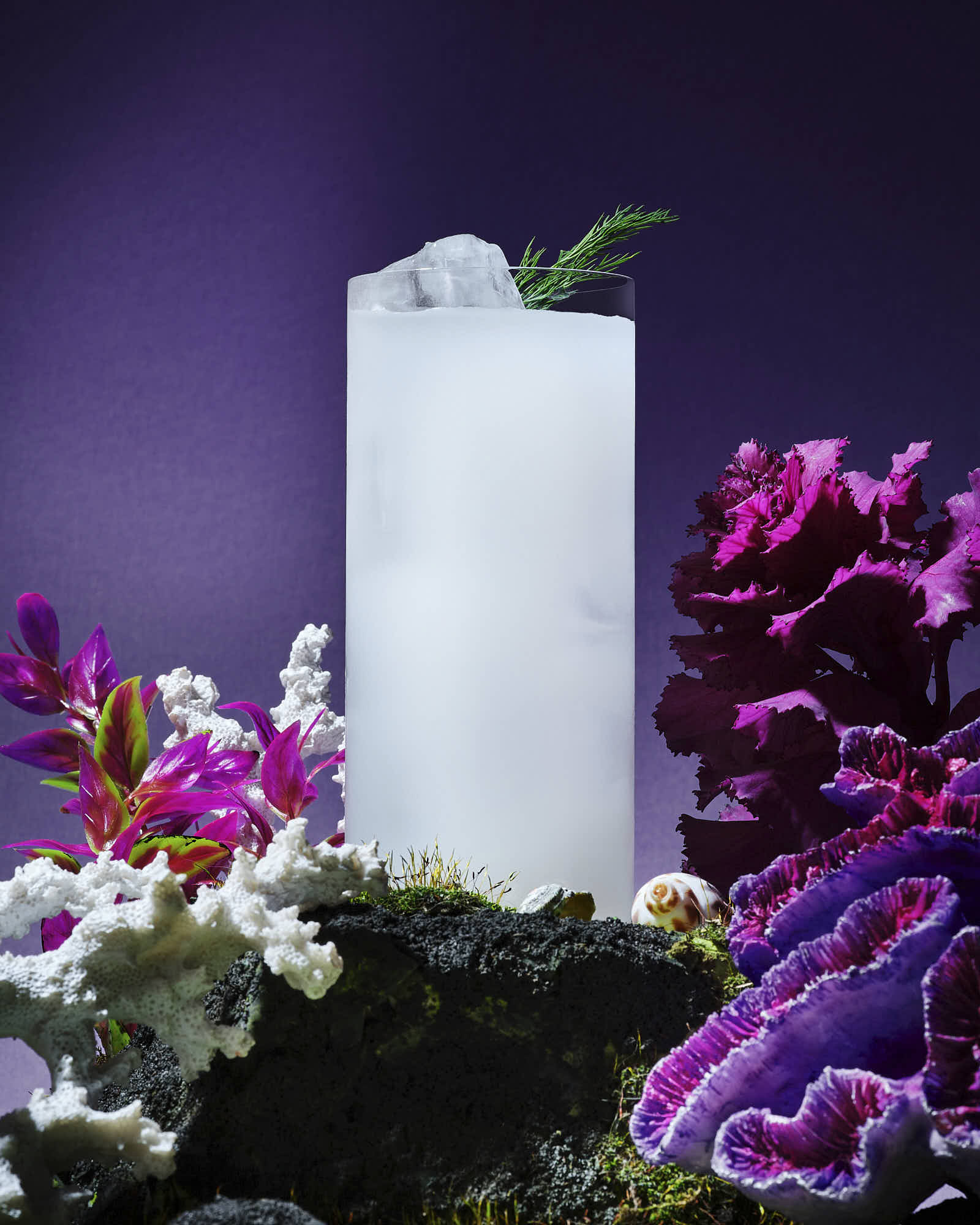 A white cocktail surrounded by colorful flowers against a purple background, creating a serene atmosphere.