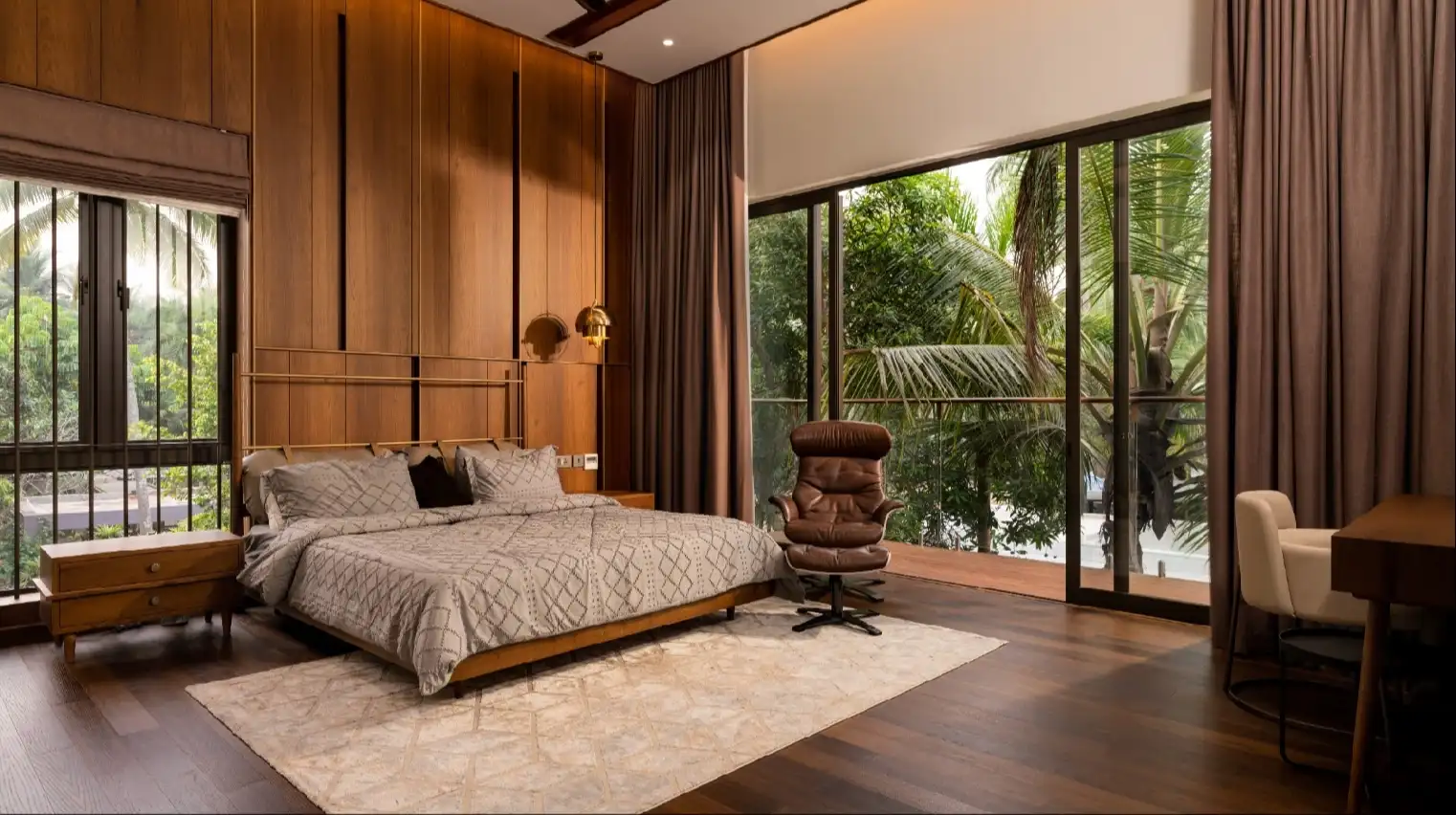 A serene and elegant spa space with wooden reclining chairs and white cushions. Golden sunlight filters through a cascading water feature, creating a peaceful atmosphere. Tropical plants and candles add to the relaxing ambiance.